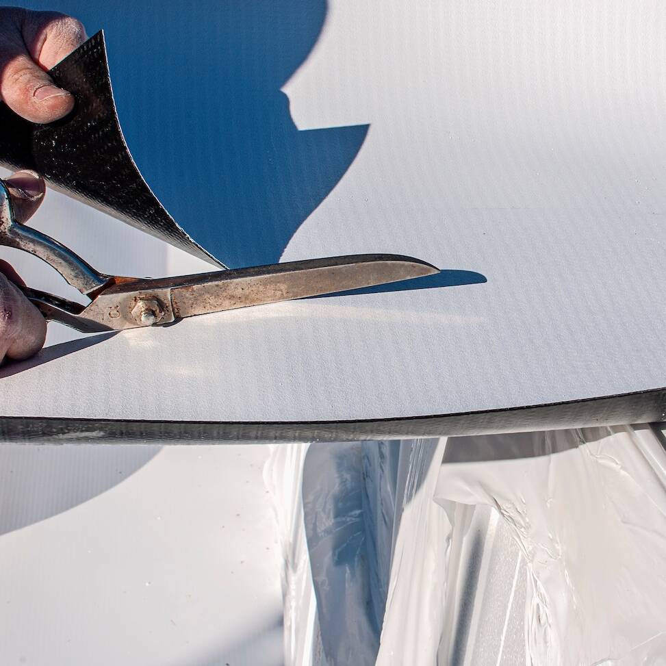 Construction worker cuts with large scissors a TPO polyolefin sheet to be applied for waterproofing a terrace of a new building