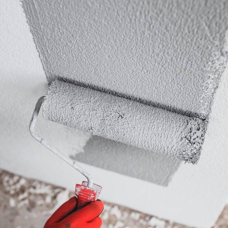 The painter paints the outer wall of the building with a gray paint roller - facade work - painting the plaster