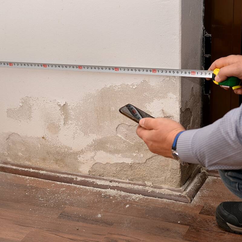 A person measures the width of a wall with visible water damage